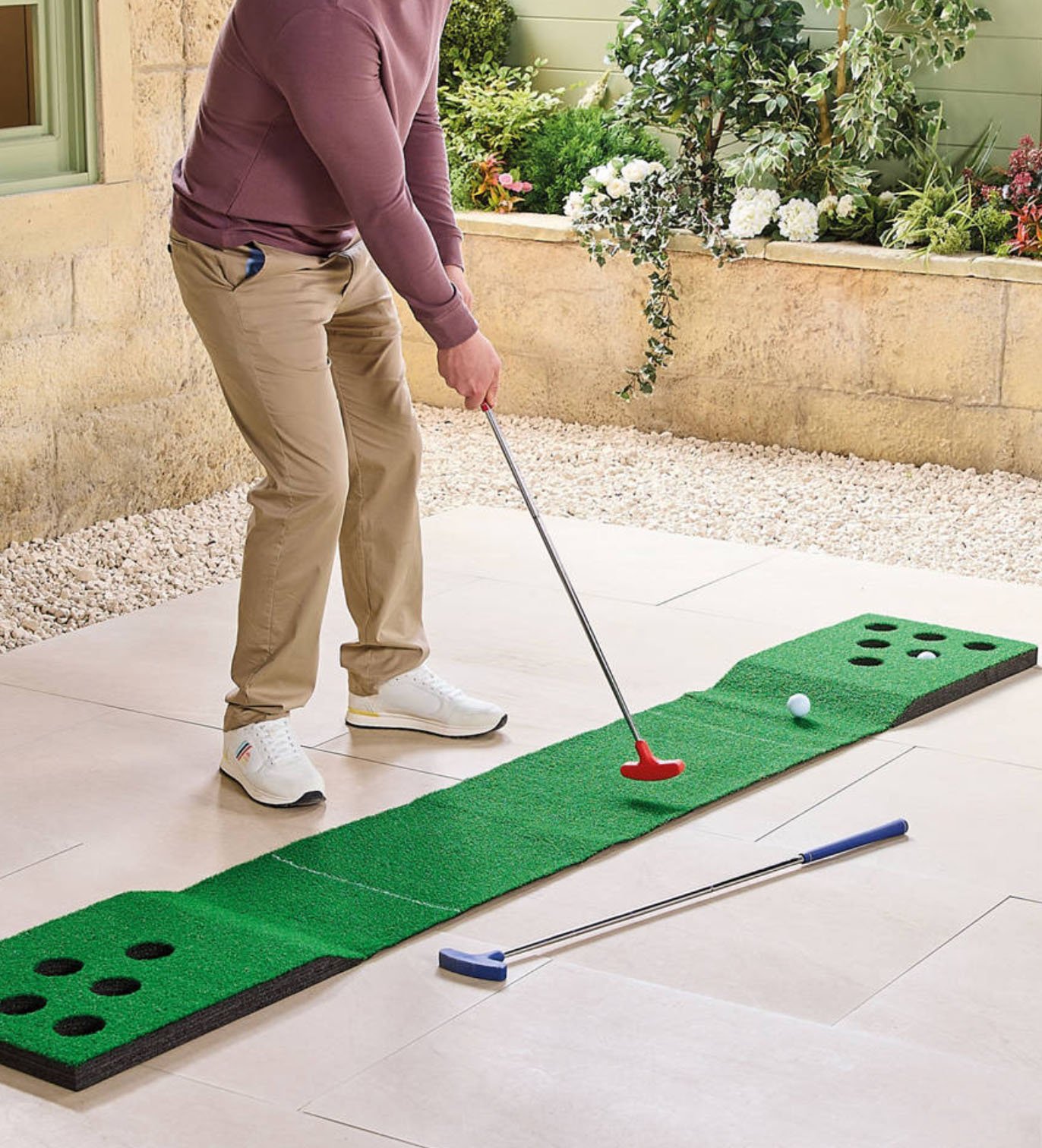 Man using a red putter to aim at a putting mat with golf pong-style targets at either end