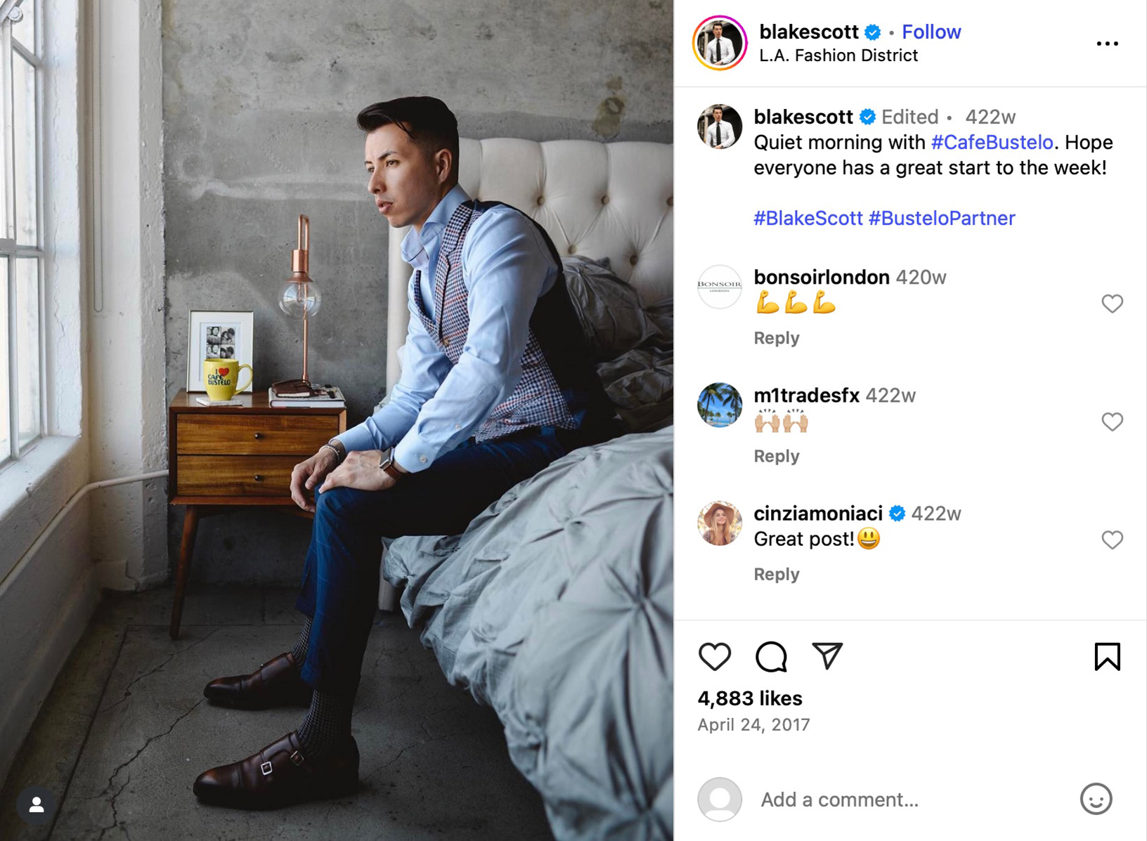 Blake Scott sitting on a bed in a tailored outfit, looking out a window with a Cafe Bustelo mug on the nightstand