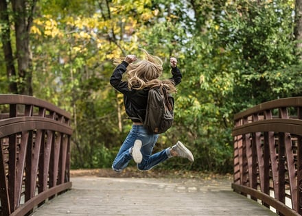 blonde-haired person jumping with both legs on a bridge