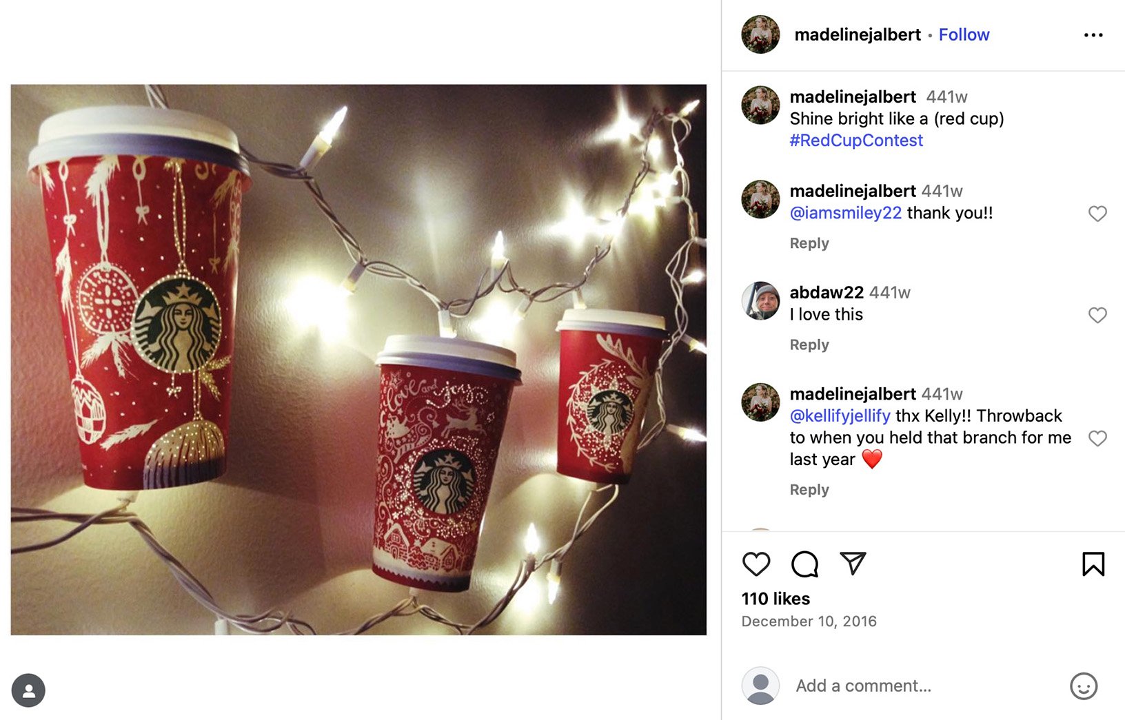 Three Starbucks red holiday cups hung on a string of fairy lights against a wall